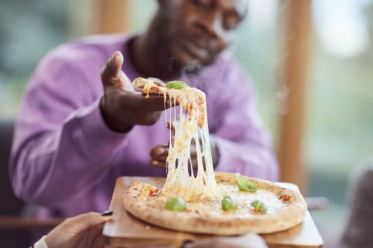 A young men enjoying a pizza with melted cheesing