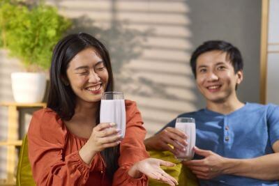 An Asian couple sitting inside, laughing and talking while drinking berry-flavored drinkable yogurt beverages