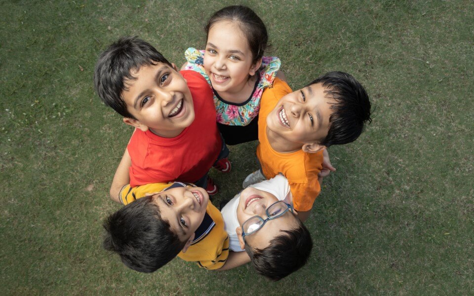 Generation Alpha children in India, standing in a circle, smiling and looking up at a camera above them
