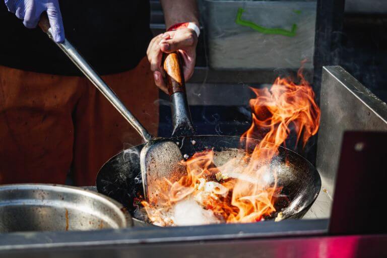 Man's hands holding a skillet, cooking food and shaking the skillet. Fire rising up off of the skillet
