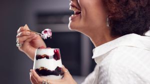 Side profile of a woman smiling and getting ready to eat a yogurt parfait with berries and granola and chocolate sauce. Her eyes are cut off but smile, neck, hands are shown
