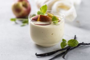 A glass of fruit- and vanilla-flavored yogurt sitting on a countertop. Fruit, herbs and vanilla are sprinkled around the glass