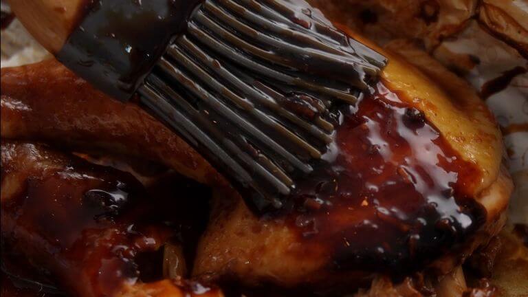 Macro shot of a basting brush applying BBQ sauce to a meat filet.