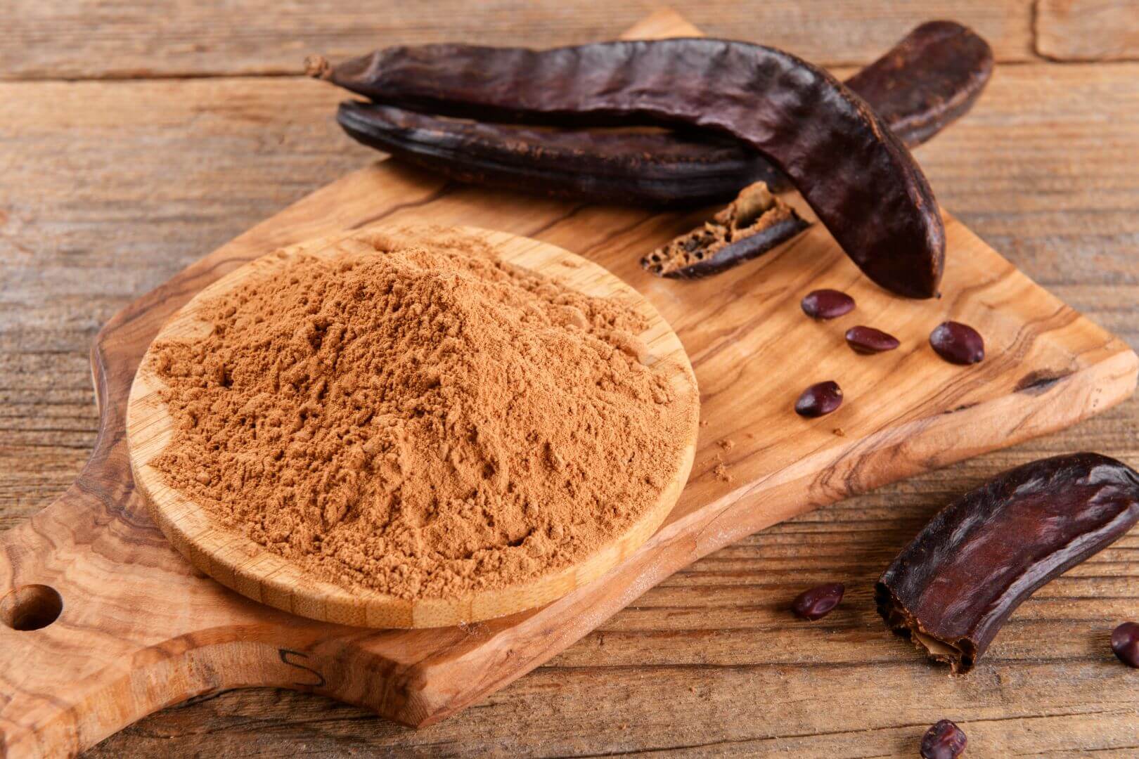 Carob pods and carob powder on a wooden board, all sitting on a wooden table