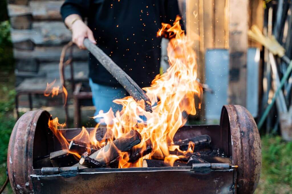 A man outside cooking barbecue on a grill, with flames rising up