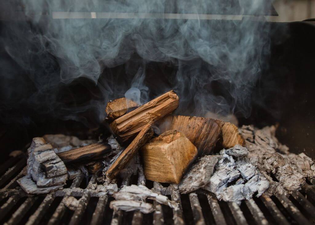 Smoke rising up from hickory wood and wood chips on a grill.