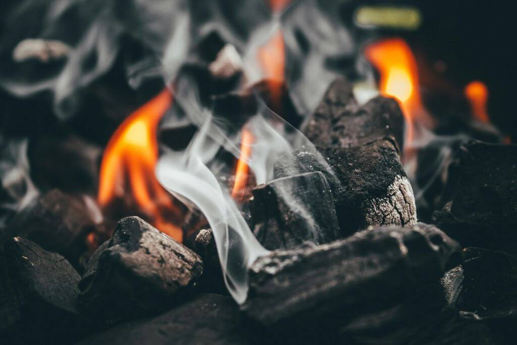 Macro shot of smoke and flames rising from wood chips and coal on a grill