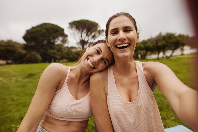 Close up of two female friends in park for a workout. Women in fitness wear relaxing and having fun after workout