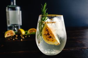 AI concept of a cocktail with rosemary sprig and charred citrus fruits. Charred fruits and bottle of liquor sitting behind the glass, too