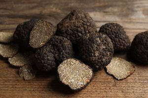 Whole black truffles and sliced black truffles all sitting next to each other on a wooden table
