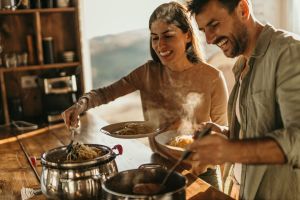Couple in the kitchen laughing and cooking over a stove. Steam rising from a pot