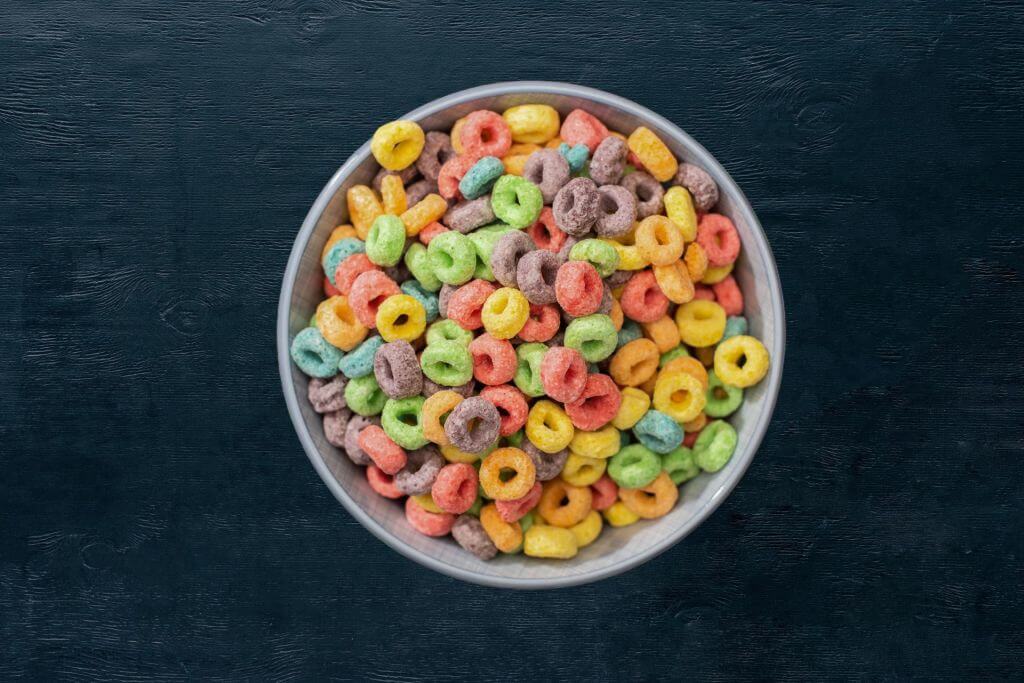 A bowl of multi-colored cereal, dyed with natural food color, on a dark surface.