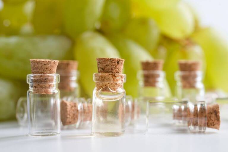 Multiple vials of a grape-based beverage, all sitting on a white table with green grapes sitting behind them