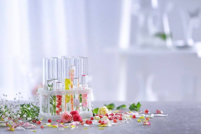 Vials with differently scented liquids and botanicals in them, surrounded by flowers on a table