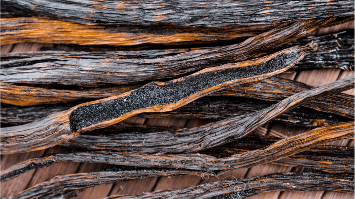 Close-up shot of vanilla beans, all lying on each other, with some cut open
