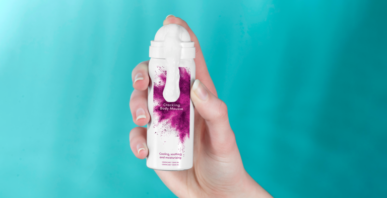 A hand holding Crackling Body Mousse against a turquoise background.